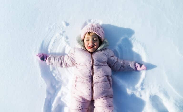 Top view portrait of cheerful small girl lying in snow in winter nature, making angels